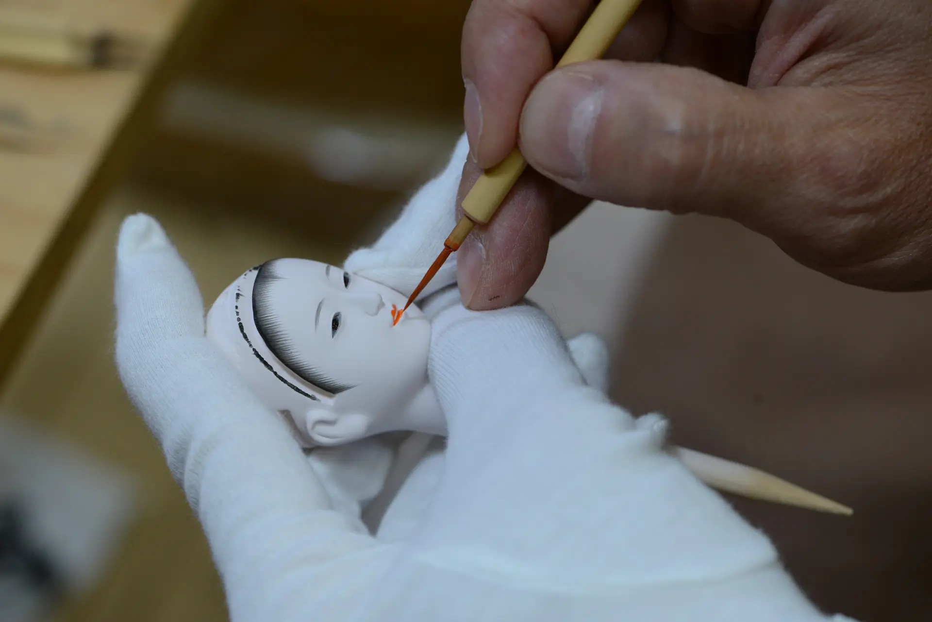 職人の手元で人形の顔に彩色を施す作業。繊細な筆づかいで表情が描き込まれる