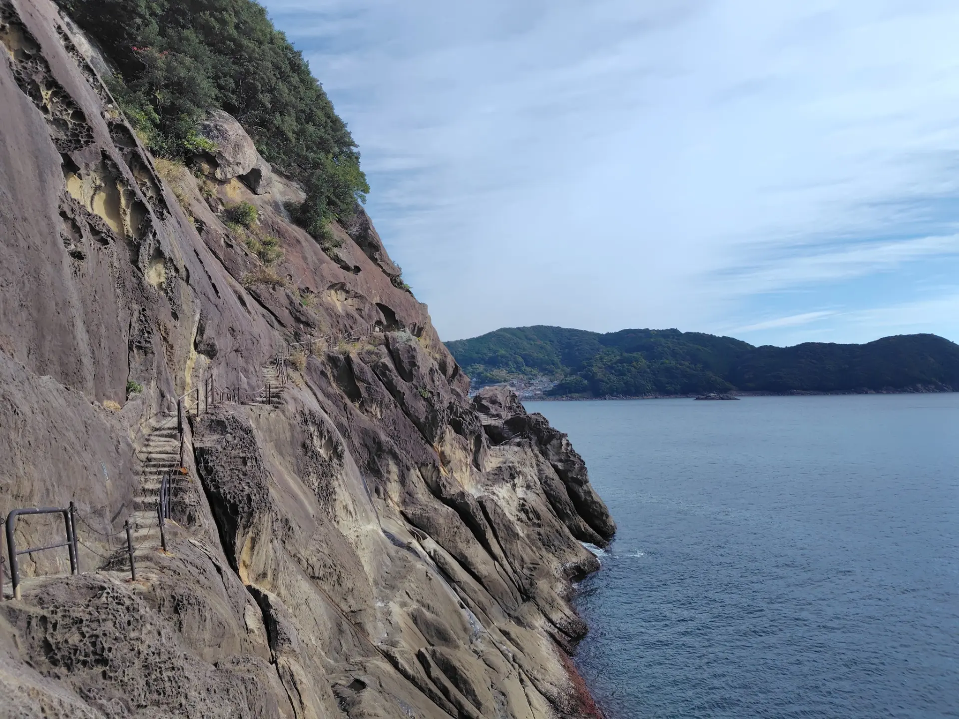 海食で削られた岩肌が連なる海岸景観。断崖に沿う遊歩道を進む