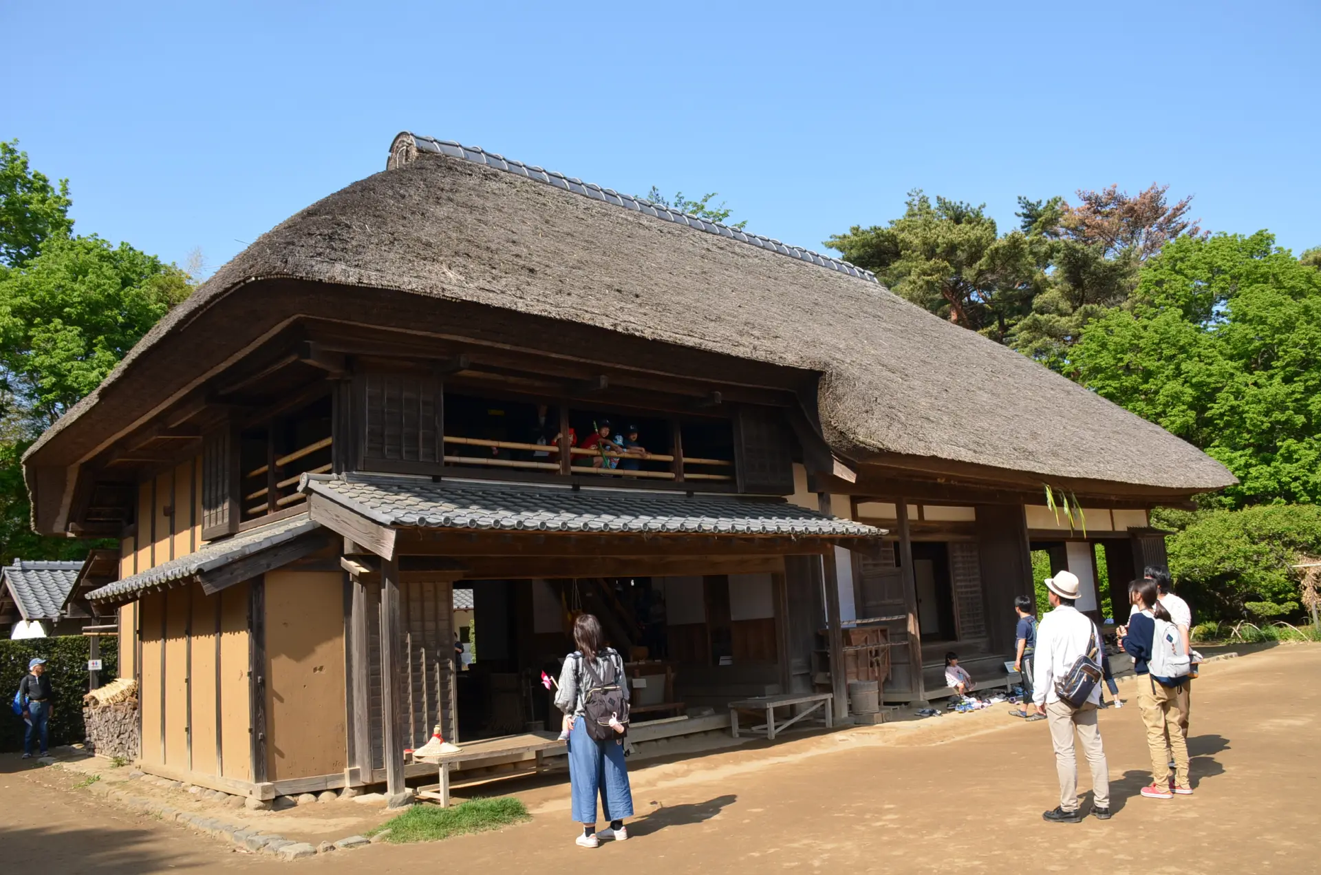 茅葺き屋根の大型民家と土間を備えた建物外観。昔の暮らしの構造が見える