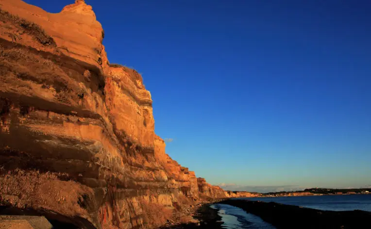 夕方の光を受けて赤く染まる崖面と海のコントラストが幻想的