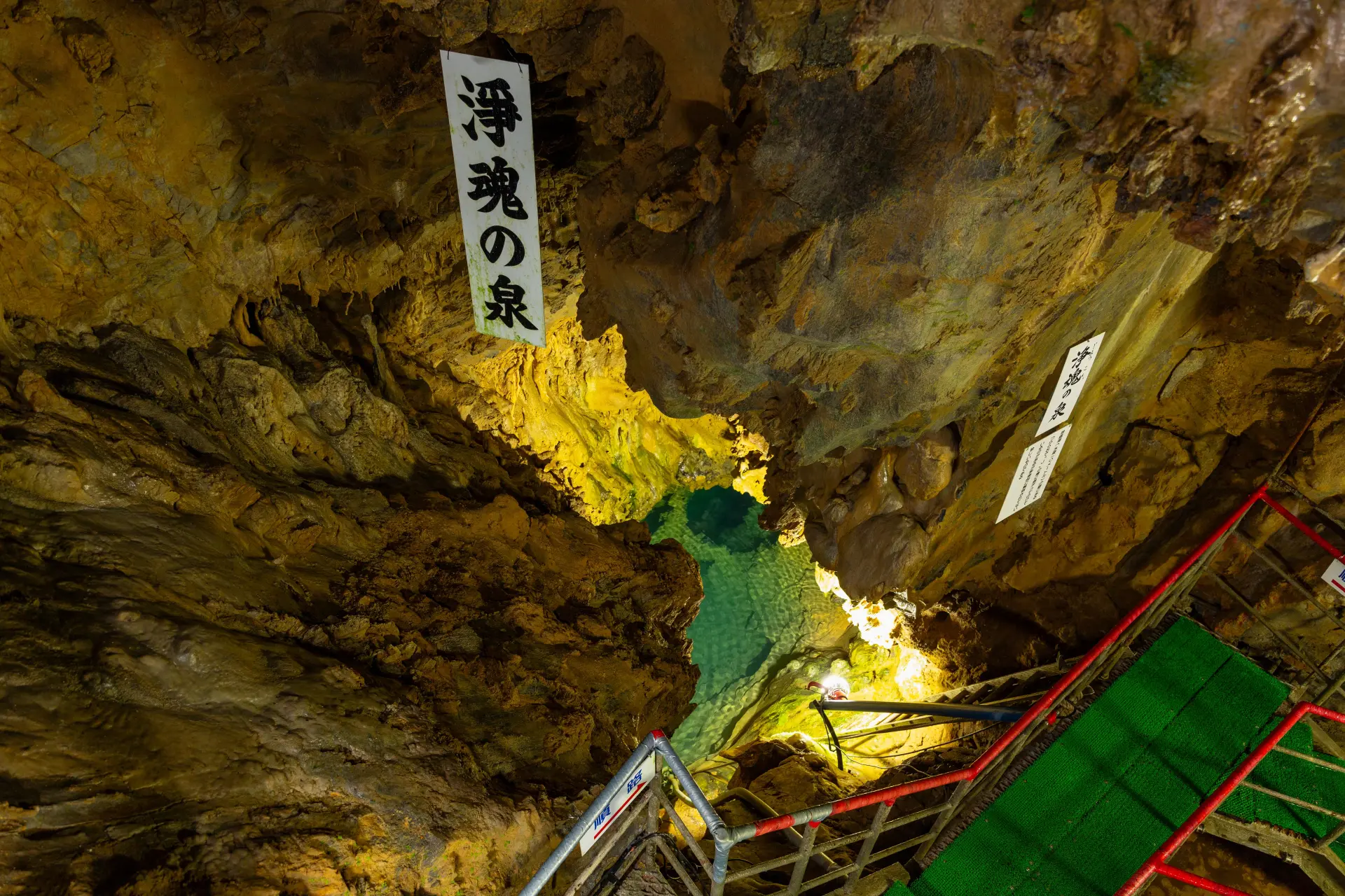 洞内の岩壁に囲まれた地底湖と階段。掲示物とともに観察できる