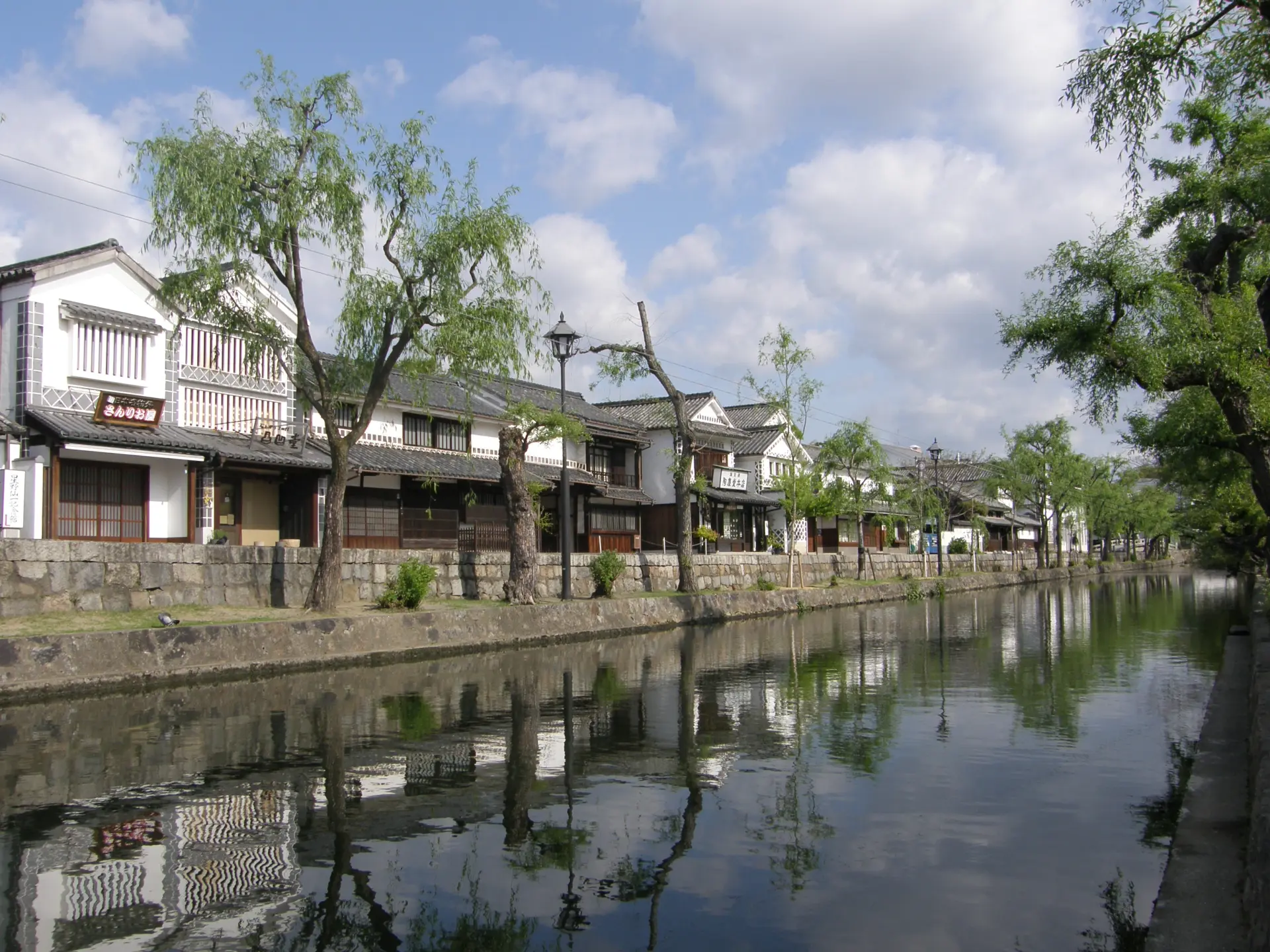 柳が揺れる倉敷川沿いの町並み。水面に映る白壁も美しい