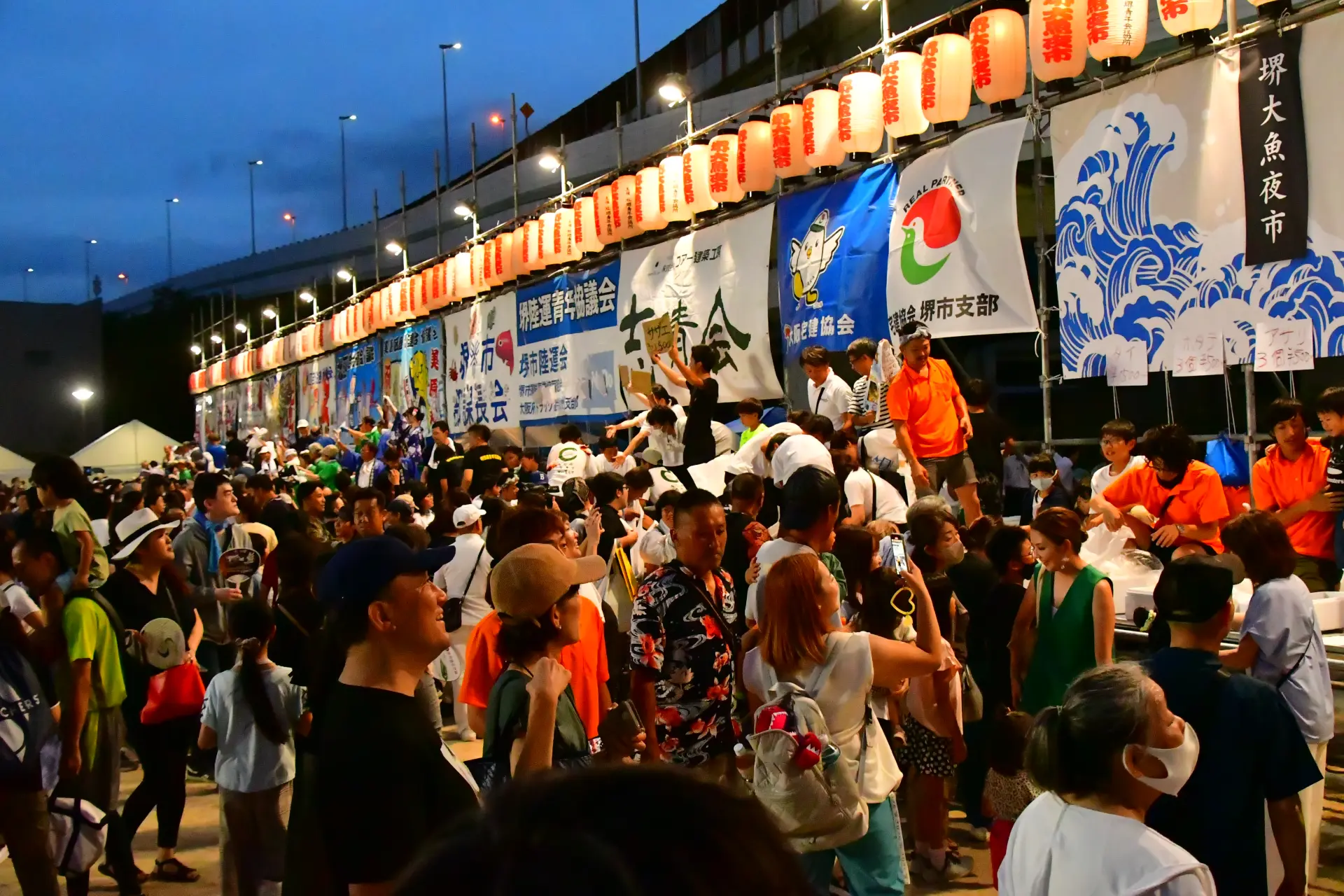 提灯が灯る会場で、多くの人が集まり活気に包まれる「魚のセリ」