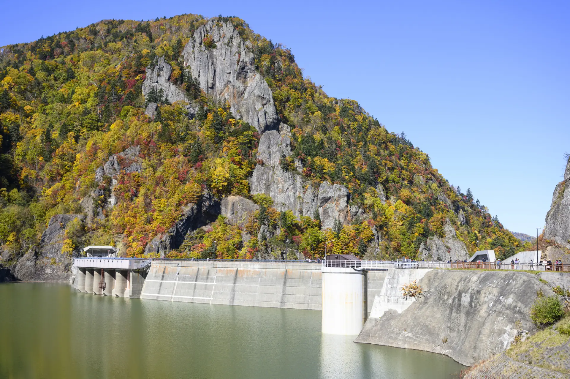 色づく山々と切り立った岩肌を背景に、ダム湖の雄大な眺めが広がる
