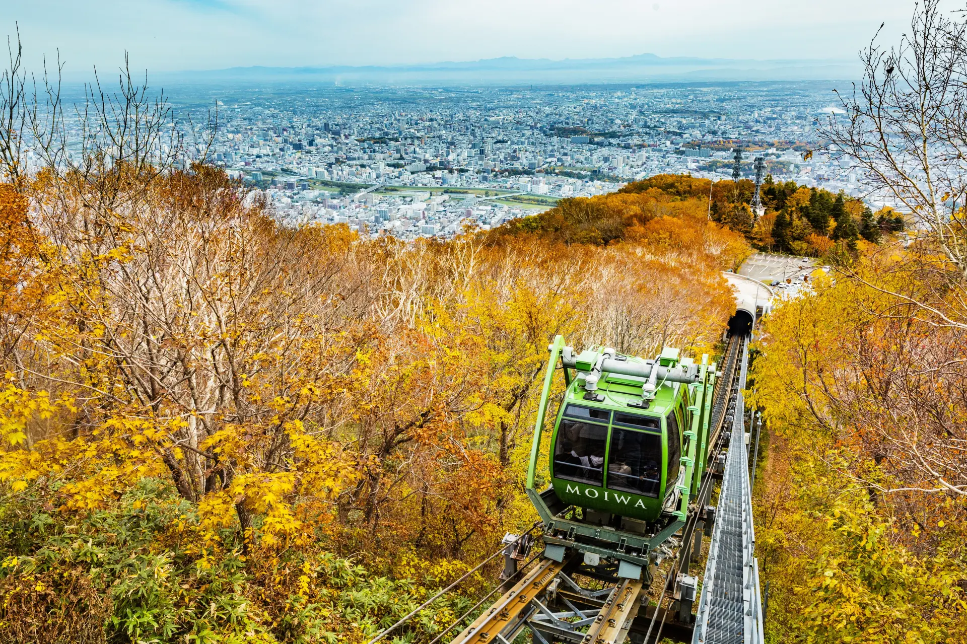 色づく木々の中を進むミニケーブルカーから、眼下に広がる市街地を望む