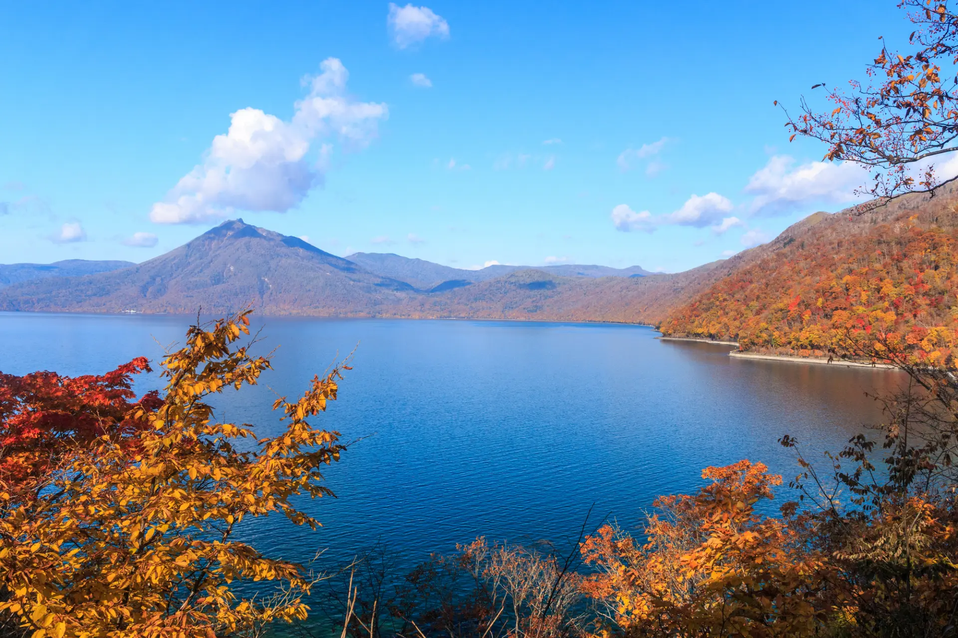 青く澄んだ湖面を囲む山々が赤や黄に色づく、秋の支笏湖