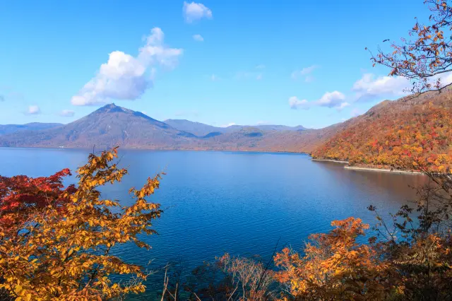 青く澄んだ湖面を囲む山々が赤や黄に色づく、秋の支笏湖
