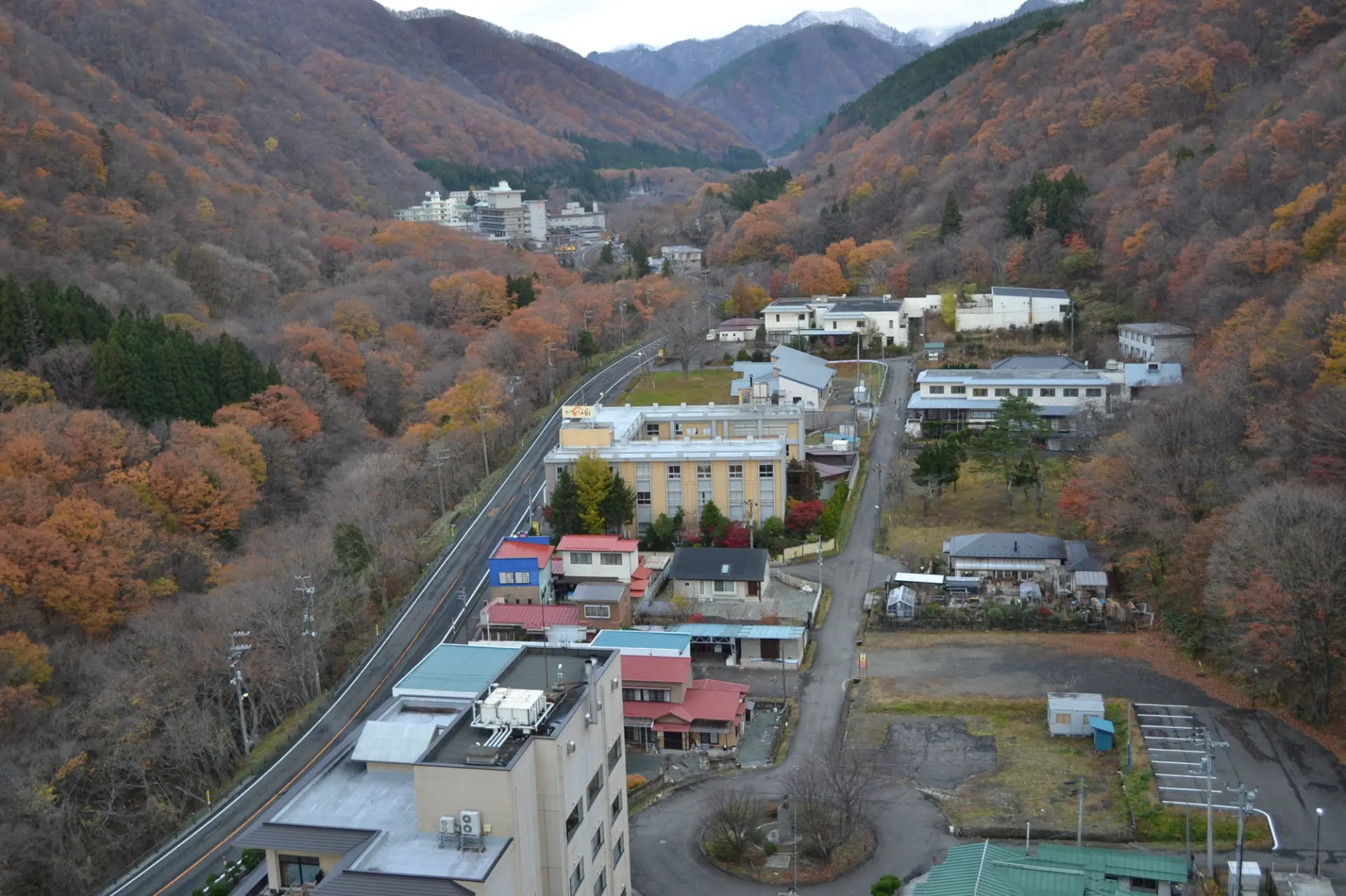 紅葉に染まる山あいに、温泉街の建物が点在する秋の景観