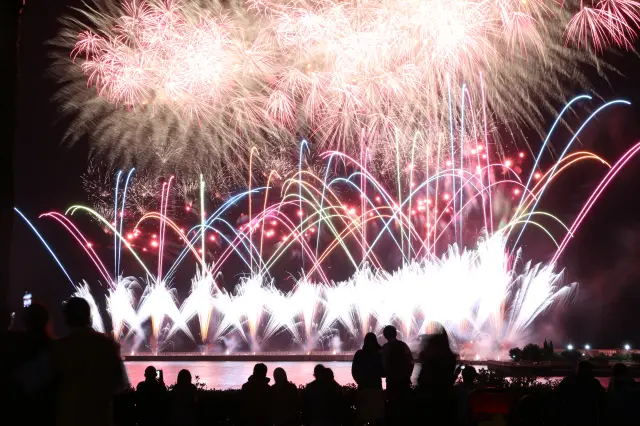 虹色の光が水面に反射する圧巻のスターマイン