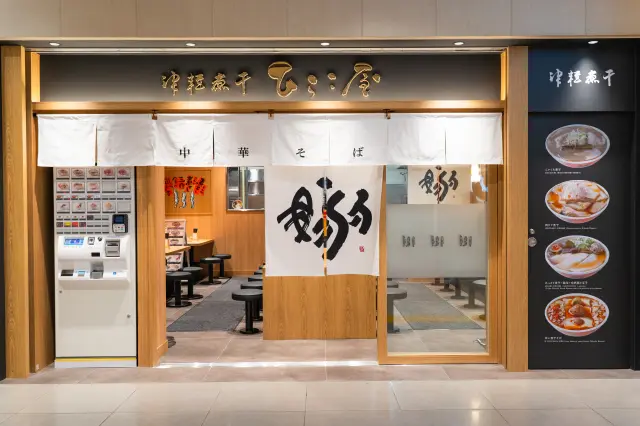 金色の店名看板と白い暖簾が目印の店舗入口
