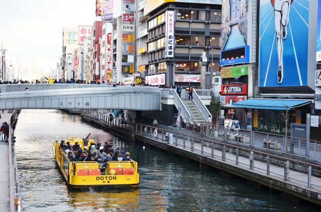 A tranquil cruise journeying through the Dotonbori River surrounded by towering buildings.